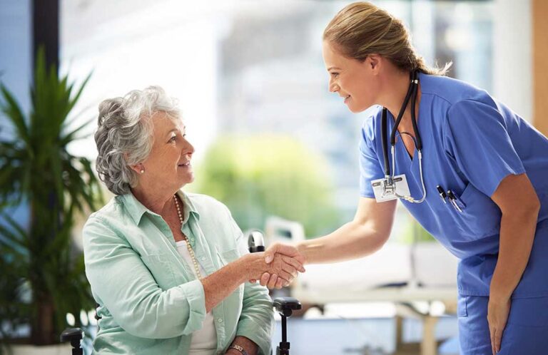 Adult daughter holding hands with her elderly mother during a visit in a cozy assisted living apartment.